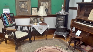 Items of clothing that would be found in a turn of the century home. There is an organ from the 1900s, a baby crib, and a bed, complete with bed warmer, which coals from the fire would be put in to make the bed nice and cozy on those cold Alberta nights.